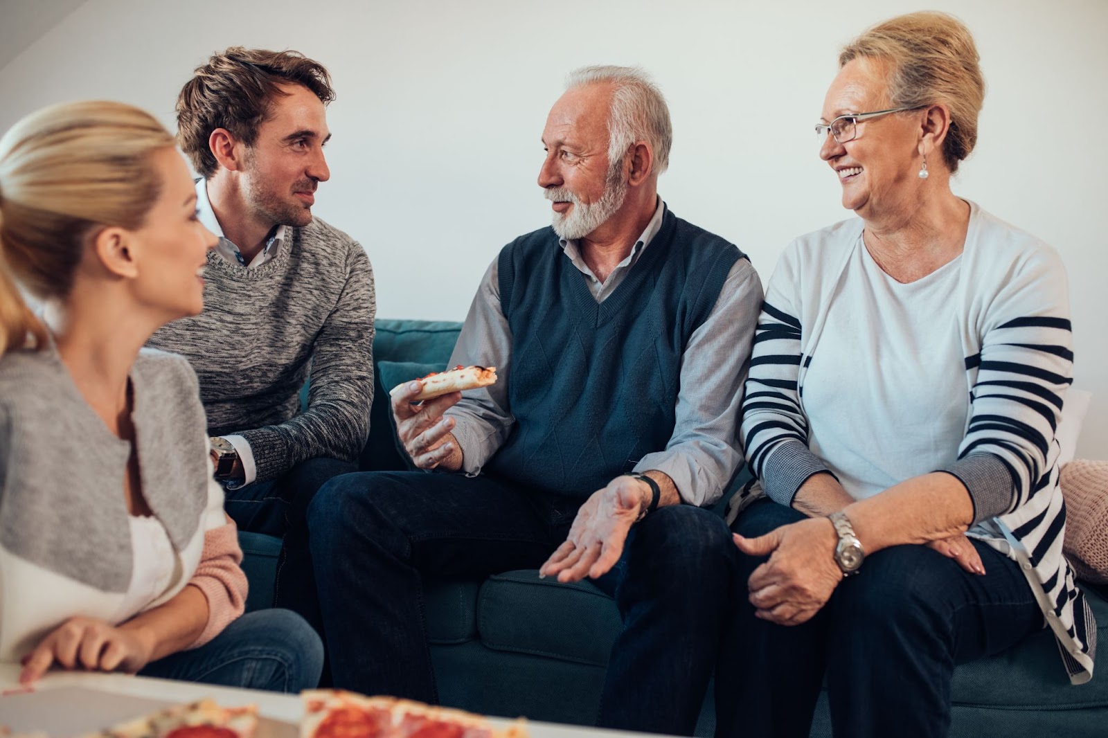 Adult children happily bond with their parents at a senior living home over pizza, sharing joyful moments and togetherness.