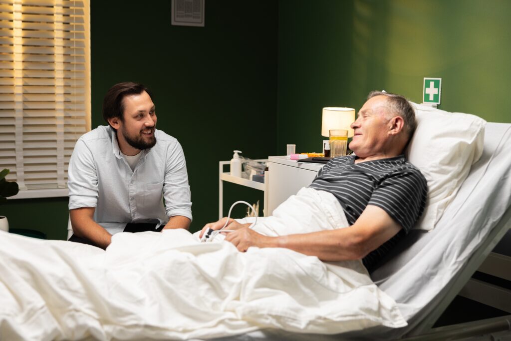 An older adult man in a long-term skilled care home enjoys a bedside visit from his son.