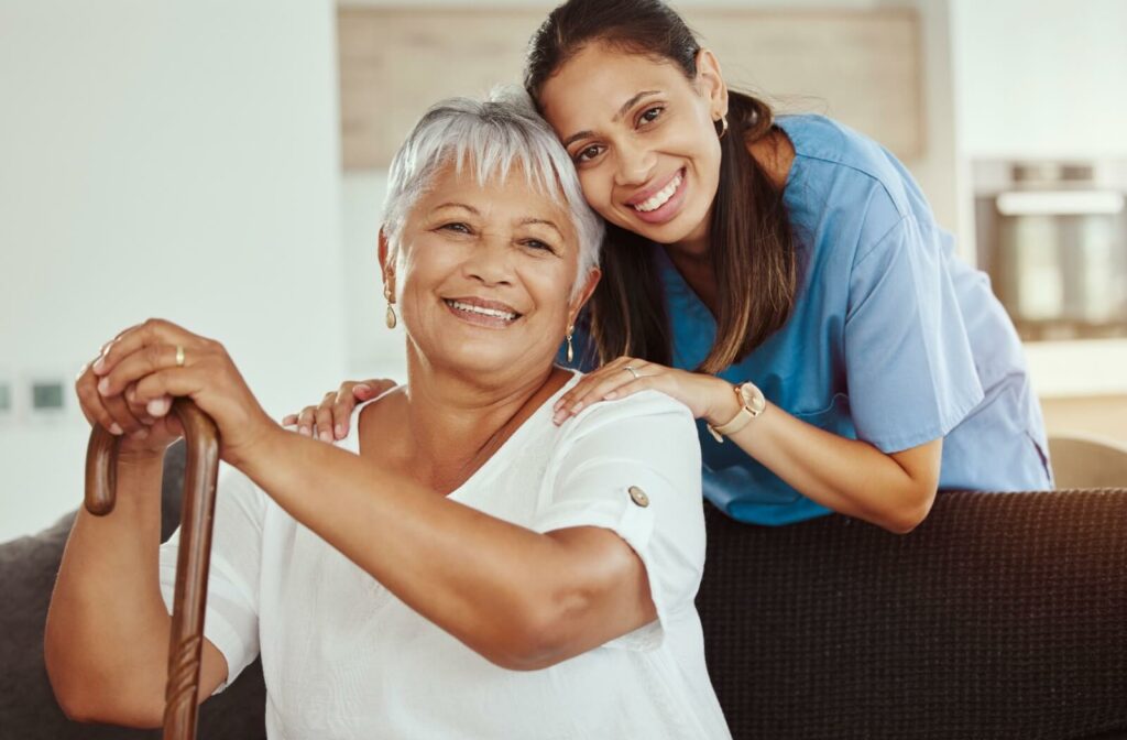 A personal care home staff member embraces a resident seated on a couch as they share a smile.