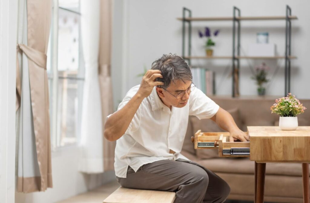 An older adult man looks puzzled as he checks his desk drawer for something.