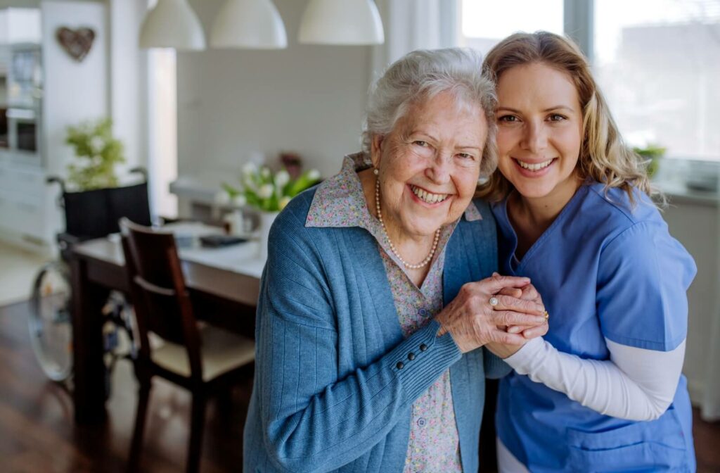 An assisted living staff member holds hands and smiles with an older adult resident.
