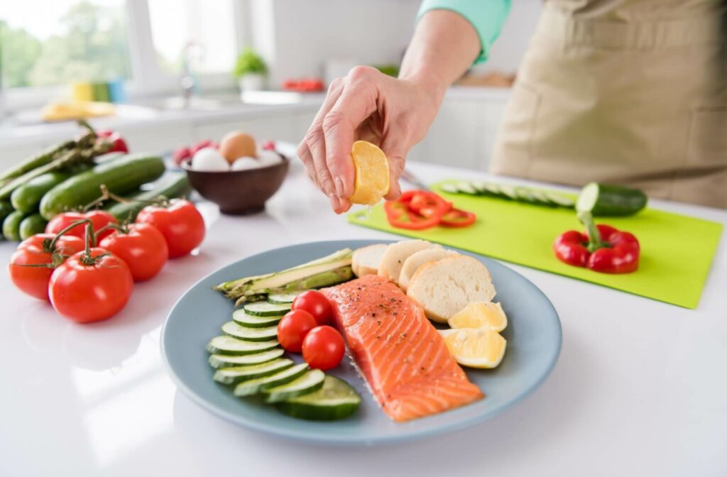 A mature woman squeezes lemon onto a plate of raw salmon and fresh veggies.