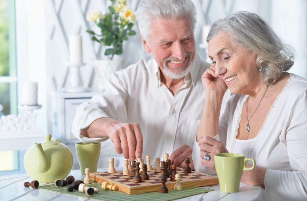 An older adult couple happily playing a game of chess with morning coffee.