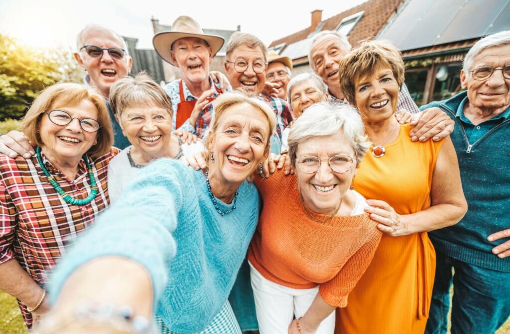 A group of older adults huddle together and smile for a selfie outside of their assisted living community.