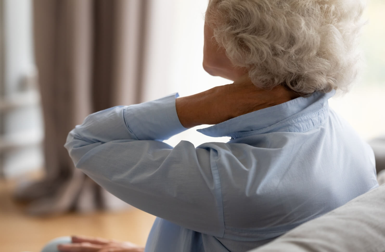 An older adult rubbing their neck in discomfort while sitting on their couch in senior living.