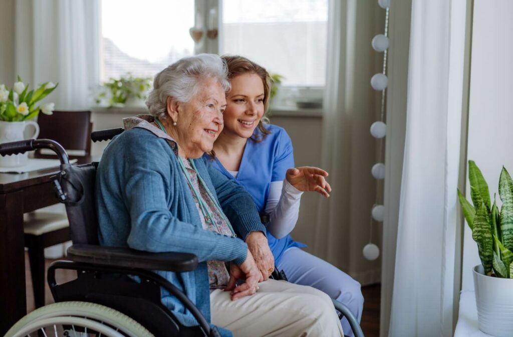 A caregiver crouching beside a smiling older resident in memory care to show them something during an afternoon activity.